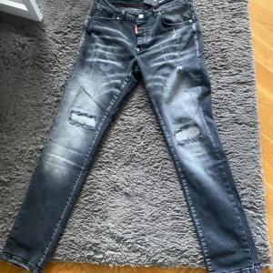 Svarta  jeans från Dsquared2 - Snygga svarta  jeans från Dsquared2 med slitningar och trasiga detaljer på knäna. Jeansen har en tvättad look med ljusare partier och klassiska fem fickor. Röd Dsquared2-tag vid fickan och coolt märke bak i midjan.