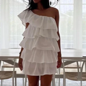 Vit volangklänning one shoulder - Superfin vit kortklänning med volanger som är oneshoulder. Klänningen är från ANIELLE och är i storlek XS, standard längd. Passar mig som är 170. Den är helt ny och lappen sitter kvar! 