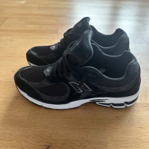 Svarta New Balance 2002r sneakers i mocka och mesh - Snygga svarta New Balance sneakers med klassisk N-logga på sidan. Ovandelen är i en mix av mocka och mesh. Skorna har snörning och en vit, mönstrad sula som ger bra grepp. Perfekta för dig som gillar streetwear och sportig vibe. Använda 3 gånger för att det är för små för min fot. Passar även för de som har storlek 47