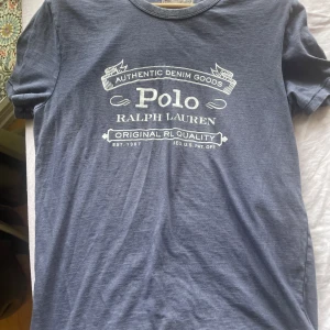 Blå t-shirt från Polo Ralph Lauren - Snygg blå t-shirt från Polo Ralph Lauren med vit tryckt logga och text på bröstet. Klassisk rund halsringning och korta ärmar. Tillverkad i mjuk bomull som känns skön mot huden. Perfekt för en avslappnad och stilren look.