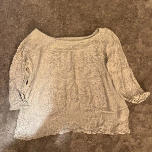 Vit prickig blus med trekvartsärm - Söt och luftig vit blus med små svarta prickar och smockad halsringning. Blusen har trekvartsärmar med lätt volang vid ärmslut och är tillverkad i ett tunt, flowy material som ger en avslappnad vibe.