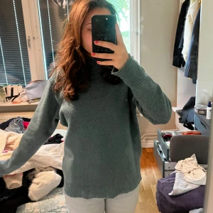 Mörkgrön stickad polotröja - Mysig mörkgrön stickad polotröja med hög krage och långa ärmar. Den är knappt nopprig .