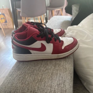 Nike Air Jordan 1 Low Chicago - Säljer ett par Nike Air Jordan 1 Low i den klassiska Chicago-färgen. Skorna har en snygg mix av rött, vitt och svart skinn, svart snörning och perforerad tåbox. Ikonisk Jumpman-logga på plösen och röd Swoosh på sidan. Perfekta för dig som gillar streetstyle. Knappt använda