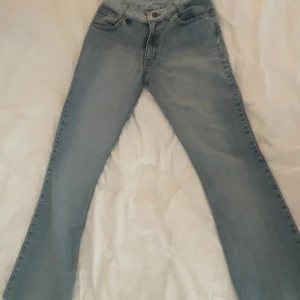 Ljusblå Levis 501 jeans bootcut - Säljer ett par klassiska ljusblå Levis 501 jeans med bootcut. Jeansen har fem fickor, knappgylf och den ikoniska Levis-lappen bak. Perfekt tvättad denim med raka ben som går ut lite nertill för en snygg siluett.