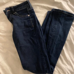 Mörkblå jeans från Divided H&M - Snygga mörkblå jeans från Divided H&M med klassisk femficksdesign och kontrastsömmar. Jeansen har bootcut och låg midja, perfekta till sneakers eller boots. Materialet är mjukt denim som sitter skönt hela dagen.