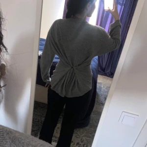 Grå stickad tröja med knäppning i midjan - Mysig grå stickad tröja med lång ärm och rund hals. Tröjan har en unik detalj med knäppning i midjan som ger en snygg draperad effekt både fram och bak. Perfekt för dig som gillar en chill men ändå stilren look. Tröjan går även att användas som en vanlig stickad tröja😊💗