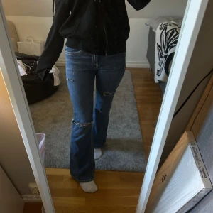Blå bootcut jeans med slitningar - Säljer ett par blå bootcut jeans med snygga slitningar på knäna och låret. Jeansen har emellan jätte low waist och high waist midja, klassiska fickor och kontrastsömmar. Perfekta för dig som gillar en avslappnad men trendig look. Aldrig använt. 