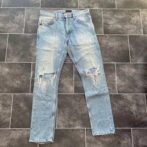 Tiger of Sweden ljusa slitna jeans - Säljer ett par ljusblå jeans från Tiger of Sweden, modell Pistolero. Jeansen har raka ben, klassisk femficksdesign och slitna detaljer med hål på båda knäna. Tillverkade i bomull och perfekta för en avslappnad streetstil.
