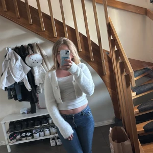 Vit fluffig kofta från Gina Tricot - Supermjuk och fluffig vit kofta från Gina Tricot. Kort, croppad modell med långa ärmar och pärlemorknappar framtill. Perfekt att slänga över ett linne eller t-shirt för en chill och trendig look.