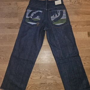Ecko Unlimited baggy jeans - Ett par mörkblå baggy jeans från Ecko Unlimited. Jeansen har raka ben och smått baggy passform, feta broderade bakfickor. Srtl 31, skulle uppskatta längden till 30. Bra skick.
