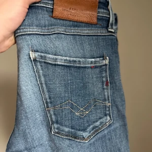 Replay Anbass slitna blå jeans - Snygga blå Replay Anbass jeans med slitningar och trasiga detaljer på benen. Klassisk femficksmodell med ljus tvätt och broderad bakficka. Sköna jeans i bomull med lite stretch för extra komfort. Slim fit. 