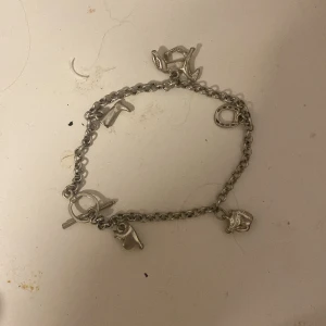 Silverfärgat cowboy charm-armband - Charmigt armband i silverfärg med flera cowboystilade berlocker som stövel, hatt, hästsko och sadel. Kedjan är grovlänkad och har ett snyggt T-lås. Perfekt accessoar för dig som gillar western vibes och unika detaljer.