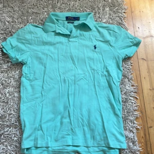 Turkos pikétröja från Ralph Lauren M - Snygg turkos pikétröja från Polo Ralph Lauren i custom slim fit. Klassisk krage, korta ärmar och den ikoniska broderade loggan på bröstet. Perfekt för dig som gillar stilrena och fräscha plagg med sportig känsla.