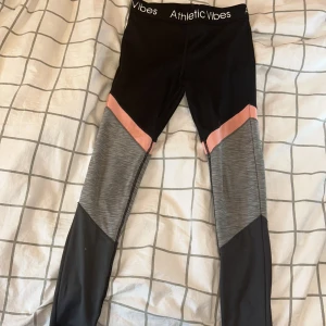 Tränings leggins - Snygga leggings från H&M sport med svart bas, gråmelerade partier och en rosa detalj vid knäna. Hög midja med logotyp i midjeresåren. Perfekta för träning eller chill, sitter tight och följer kroppen. Materialet är stretchigt och andas bra. I stl 134/140 (texten har suddats bort där storleken står så det går ej att få med på bild)