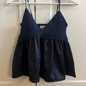 Mörkblå linnetopp från Designbyamor - Supersöt mörkblå linnetopp från Designbyamor med smala axelband och v-ringning. Överdelen är ribbad och ger en snygg kontrast till den glansiga, vida nederdelen. Perfekt för dig som gillar en luftig och trendig look.