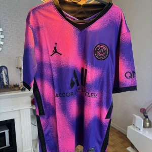 PSG x Jordan 2020/21 Special Kit - Snygg PSG fotbollströja i samarbete med Jordan. Tröjan har ett unikt lila och rosa mönster med svarta detaljer, klubbmärke och Jordan-logga på bröstet. Tillverkad i lätt och ventilerande polyester, perfekt för match eller träning. V-ringad hals och korta ärmar.