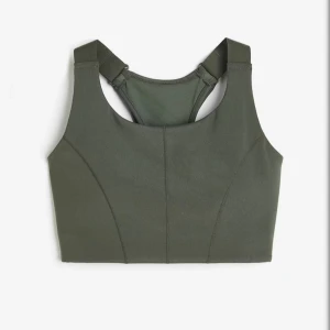 Khakigrön sport topp - Mörk khakigrön sport topp med breda axelband, justerbara spännen, ”bh-knäppning” och uttagbara ”pads”. Tillverkad i stretchigt syntetmaterial som andas, perfekt för aktiva dagar och träning. Nästan helt slutsåld på hemsidan. Säljer pga lite användning, använd ca 2 ggr.🥰