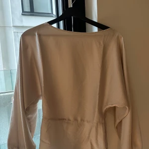 Champagnefärgad långärmad blus H&M XS - Champagnefärgad långärmad blus H&M XS. Har lång ärm, rak passform och är tillverkad i ett lätt, satinliknande tyg. Perfekt för dig som gillar minimalistisk och clean stil. Intagen midja som ger snygg passform 