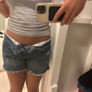 Blå jeansshorts med fransig kant - Snygga blå jeansshorts med fransig kant och slitna framtill. Storleken är 34