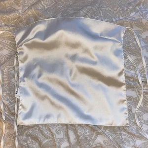 Champagnefärgad satin tubtopp med snörning - Säljer en glansig champagnefärgad tubtopp från NA-KD i satin. Toppen är bandeau-modell och har snygga snörningsdetaljer i ryggen som gör att du kan justera passformen. Perfekt för dig som vill sticka ut med en elegant och trendig look.