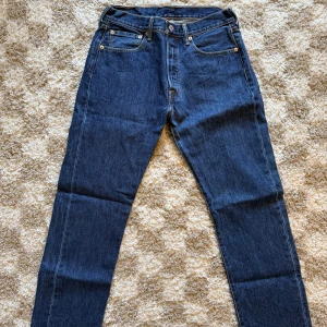 Levi's 501 jeans W31 L30 - Klassiska Levi's 501 jeans i mörkblå denim. Rak passform med fem fickor, knappgylf och snygga kontrastsömmar. Ikonisk läderpatch bak i midjan och röd Levi's-tagg på bakfickan.