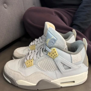 Nike Air Jordan 4 Retro ljusgrå - Nike Air Jordan 4 Retro i ljusgrå och beige toner med detaljer i gult. Ovandel i mocka och skinn, meshpaneler på sidorna och klassisk Jumpman-logga på häl och plös. Grå och vit sula med synlig Air-enhet. Perfekta för dig som gillar streetwear och sneakers med unik vibe. Bra skick har tagit hand om den väldigt bra 