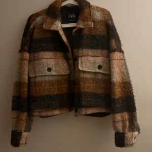 Rutig teddyjacka från Zara i bruna toner - Säljer en supermjuk och mysig teddyjacka från Zara i storlek S (den är lite oversized) Jackan är rutig i bruna, beige och svarta nyanser, har stora fickor framtill med knappar och klassisk krage. Har använt flera gånger men fortfarande i en väldigt bra skick. 