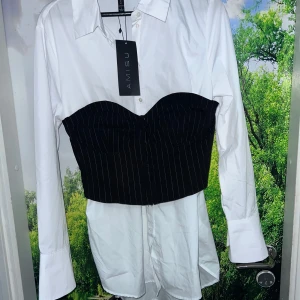 Fashion statement! Ny skjorta med inbyggd korsett från Amisu - Stilren och modern vit skjortklänning med fastsydd svart korsett-detalj. Kan bäras som en lång skjorta, klänning eller stylas med byxor – supermångsidig! Skjortan är i bomull. Köpt på New Yorker                                                        Skick: Aldrig använd, prislappen sitter kvar – helt ny!     Skriv gärna innan du trycker på köp nu 