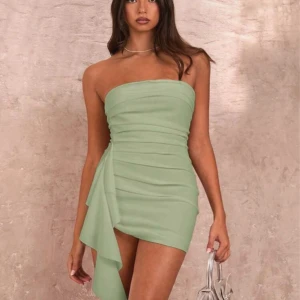 Ljusgrön axelbandslös klänning - Superfin ljusgrön axelbandslös kortklänning med draperad design och volangdetalj på sidan. Klänningen har en tight passform men är större i storlek: Materialet känns lätt och flowy. Den är i väldigt bra kvalitet men passade tyvärr inte på mig och därför säljer jag den. Aldrig använt innan 