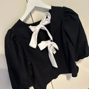 Svart blus med vita rosetter - Svart blus från H&M i storlek S, normal i storlek! Aldrig använd. Svart framsida med vita rosetter bak i ryggen. 