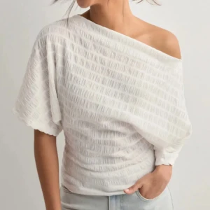 Vit offshoulder blus med struktur - Säljer en vit blus med snygg struktur och offshoulder-design. Toppen har korta ärmar och en lös passform upptill som smalnar av vid midjan. Perfekt för dig som gillar en stilren och trendig look.