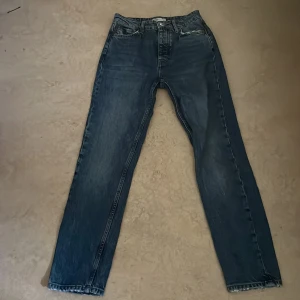 Blå jeans från Gina Tricot, rak modell - Säljer ett par klassiska blå jeans från Gina Tricot i rak modell. Jeansen har hög midja, knäppning med fyra silverfärgade knappar och fem fickor. Snygg tvätt med lätt slitning och raka ben. Perfekta till sneakers eller boots.