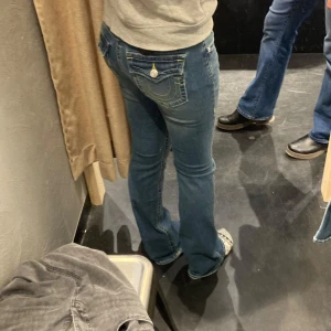 Blå bootcut jeans med broderade fickor - Säljer ett par snygga blå jeans med bootcut-modell och broderade bakfickor med gul och vit söm. Jeansen har låg midja.