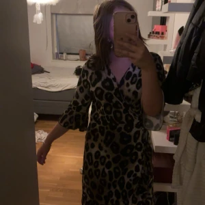 Leopardmönstrad omlottklänning - Snygg leopardmönstrad omlottklänning med v-ringning och trekvartsärm. Klänningen har svart och beige mönster i leopard och är i ett väldigt mjukt material. Perfekt för dig som vill sticka ut med ett djurmönster och gillar trendiga detaljer. Säljer då jag tycker den är lite stor för mig och blir inte till användning när jag inte känner mig bekväm i den🩷osäker på varumärket så stämmer möjligtvis inte med att den kommer från SHEIN. Ps klänningen går ner till nian knäskålar och jag är 170 mc lång. 