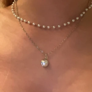Silverfärgat pärlhalsband i lager - Tvådelat halsband i silverfärg med en kedja dekorerad med små vita pärlor och en tunnare kedja med en större rund pärlberlock. Helt nytt🫶🏼💕