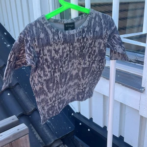 Gråmönstrad t-shirt från Blingo - Säljer en grå t-shirt från Blingo med unikt abstrakt mönster i mörkgrått och ljusgrått. Tröjan har rund halsringning och korta ärmar, perfekt för en chill och avslappnad stil. Tillverkad i mjuk bomull som känns skön mot huden.