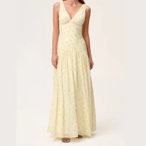 Ljusgul adoore klänning - Toulouse - Superfin långklänning i ljusgul ton med små gula blommor och gröna detaljer. Klänningen har v-ringning både fram och bak, är ärmlös och har en flowy kjol med lätt rynk. Perfekt för sommarens alla tillfällen. Använd endast en gång och är i nyskick.