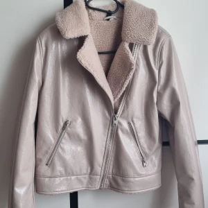Beige teddyjacka från H&M med dragkedja - Säljer en beige teddyjacka från H&M i storlek S. Jackan har glansig utsida i syntetmaterial och mjukt teddyfoder på insidan och kragen. Två snedställda fickor med dragkedja framtill och klassisk bikerstil. Perfekt för kyliga dagar!