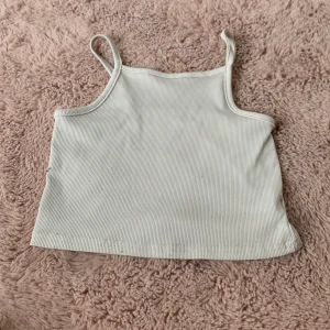 Vit ribbad croppad linnetopp - Säljer en vit croppad linnetopp med smala axelband och ribbad struktur. Toppen är tillverkad i stretchigt material med 95% polyester och 5% elastan, vilket gör den bekväm och följsam. Perfekt för en avslappnad och trendig look.