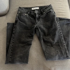 Svarta straight jeans med tvättad look - Säljer ett par svarta jeans med tvättad finish och klassisk femficksdesign. Jeansen har rak passform och låg midja, perfekta för en avslappnad stil.