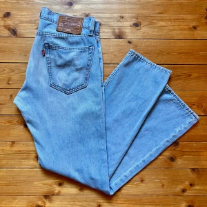 Levi's 501 ljusblå jeans straight fit - Klassiska Levi's 501 jeans i ljusblå denim med raka ben och normal passform. Byxorna har fem fickor, knappgylf och den ikoniska läderpatchen bak i midjan. Perfekta för en avslappnad och tidlös stil.