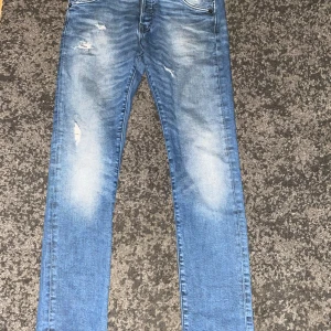 Jack and Jones   - Säljer ett par blå jeans med slitningar och snyggt tvättad look. Jeansen har fem fickor, låg midja och smal passform. Perfekta för dig som gillar en lite ruffare stil. Materialet är klassisk denim i bomull.