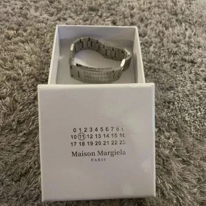 Maison Margiela ”Watch Strap Bracelet” Armband - Säljer ett stilrent och unikt armband från Maison  Margiela, Paris.  Detta är ett armband med den ikoniska sifferlogotypen där "11" är markerad - vilket står för Margielas accessoarkollektion.  Material: Rostfritt stål  Färg: Silver  Skick: Nära nyskick, endast testad  Levereras i originalskick  Perfekt för dig som en elegant minimalistisk, lyxig design med ett statement. Passar både herr och damer