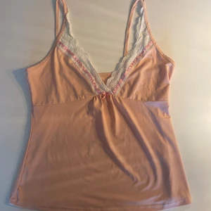 Ljusrosa  linnetopp med spets - Sött ljusrosa linnetopp med smala axelband och v-ringning.💕 Toppen har vit spets och rosa band längs ringningen samt en liten rosett framtill. Mjuk och stretchigt matrial💕säljer då det är lite för stort för mig💕