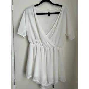 🤍Vit omlottplaysuit från H&M Divided – Strl 42 🤍 - Perfekt för sommarens varmaste dagar!☀️  Säljer en söt och svalkande playsuit från H&M Divided i en tidlöst vit nyans. Playsuiten har en smickrande omlottdesign med V-ringning, korta ärmar och resår i midjan som ger en fin siluett och bekväm passform. Shortsens nederkant är dekorerad med vackra spetsdetaljer som ger ett feminint och romantiskt intryck. Tyget är lätt och luftigt, men plagget är helfodrat så det är inte genomskinligt.✨