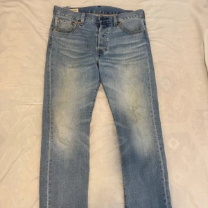 Levi's 501 ljusblå jeans W30 L30 - Klassiska Levi's 501 jeans i ljusblå tvätt med raka ben och snyggt slitna detaljer. Jeansen har fem fickor, knappgylf och den ikoniska läderpatchen bak. Perfekta för dig som gillar en tidlös och avslappnad look.