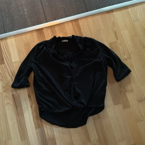 skjorta med trekvartsärm - Stilren svart skjorta. Skjortan har trekvartsärmar och en lös passform med klassisk krage. Perfekt för dig som gillar en enkel men elegant look.