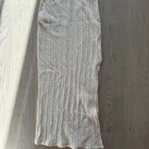 Vit långkjol från NA-KD med slits - Långkjol från NA-KD i beige med ribbad struktur och diskreta lodräta ränder. Kjolen har en snygg slits i sidan och är gjord i ett lätt, luftigt material som känns perfekt för varmare dagar. Något genomskinlig, då det är så modellen ser ut