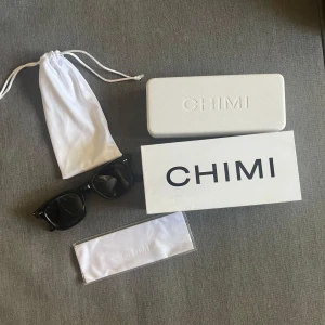 Svarta solglasögon från CHIMI - Snygga svarta solglasögon från CHIMI med klassisk, fyrkantig form och blanka bågar. Kommer med originalfodral, tygpåse och putsduk. Perfekta för att lyfta din stil och skydda ögonen mot solen.