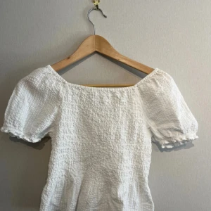 Vit smockad blus med puffärm - Supersöt vit topp/blus med smockat tyg och puffiga korta ärmar. Använd ett fåtal gånger. Köpt på Kappahls barnavdelning i storlek 158/164 men motsvarar XS